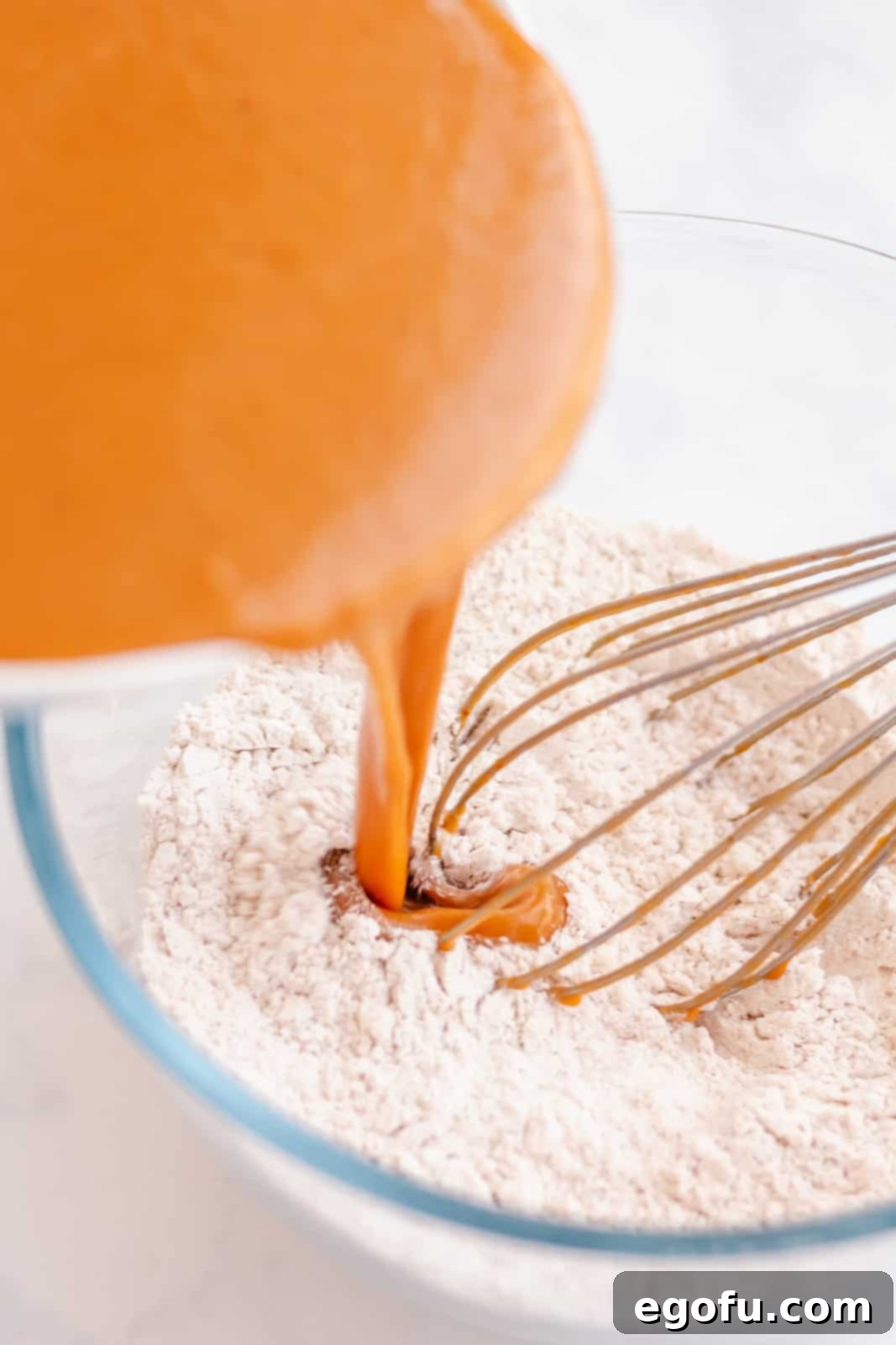 Wet ingredients being carefully poured into a bowl containing dry ingredients, signaling the next step in batter preparation.