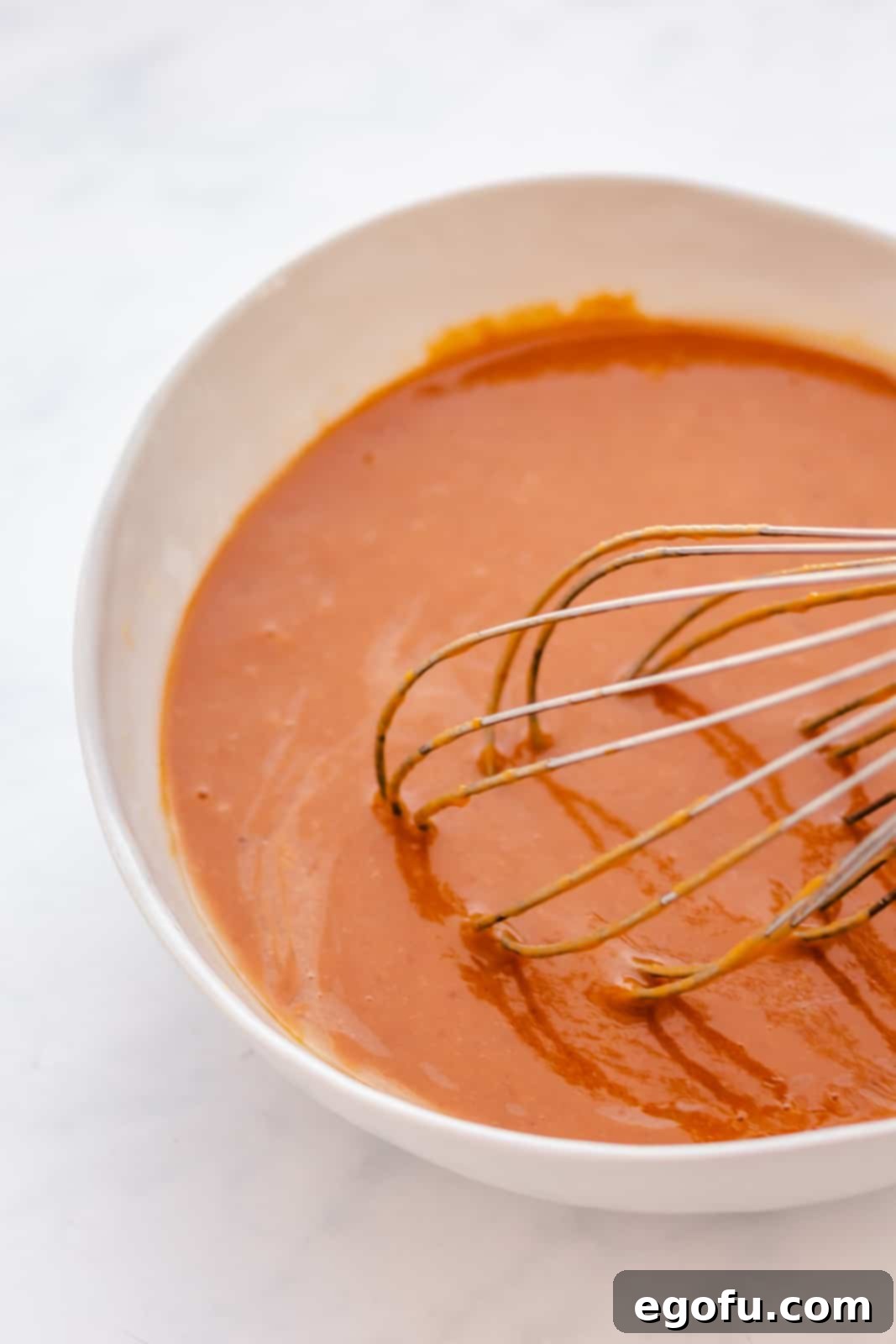 The donut batter, a smooth mixture of wet and dry ingredients, thoroughly whisked together in a bowl, ready for piping.