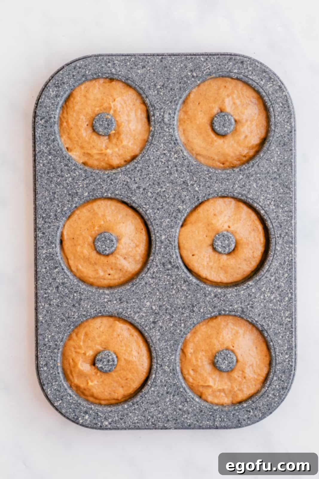 Donut batter neatly piped or spooned into the individual cavities of a donut pan, filling them approximately halfway.