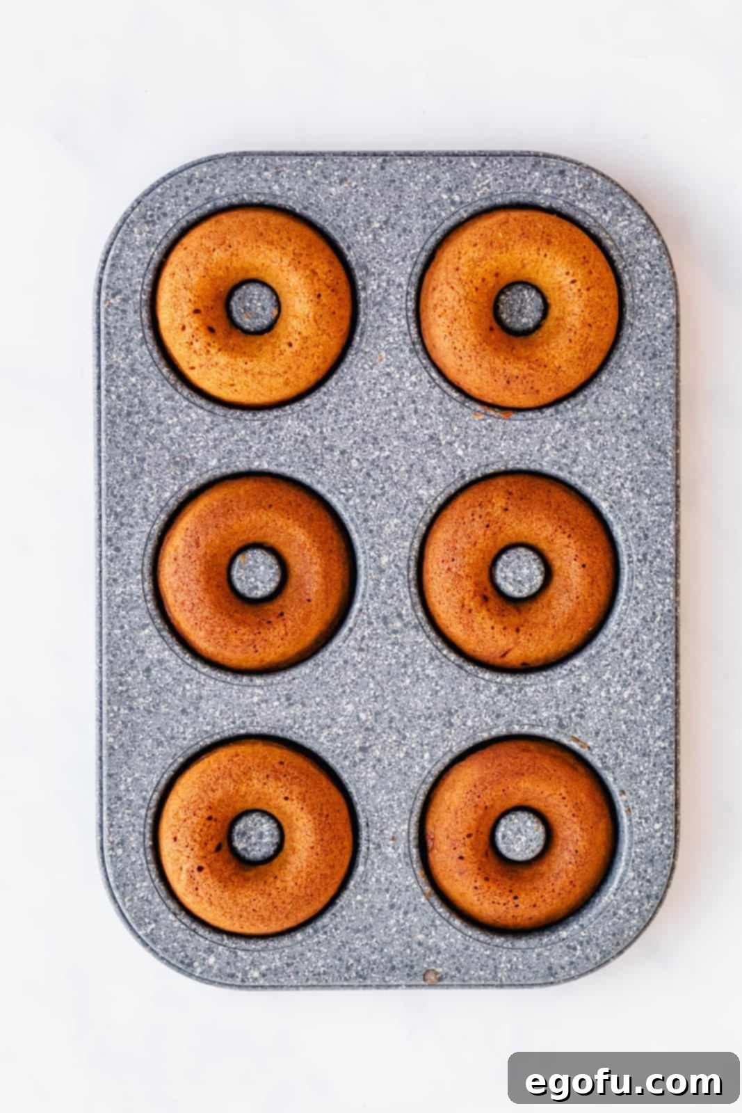 Freshly baked donuts, lightly browned and perfectly risen, cooling in a muffin pan (or donut pan), showcasing their readiness.