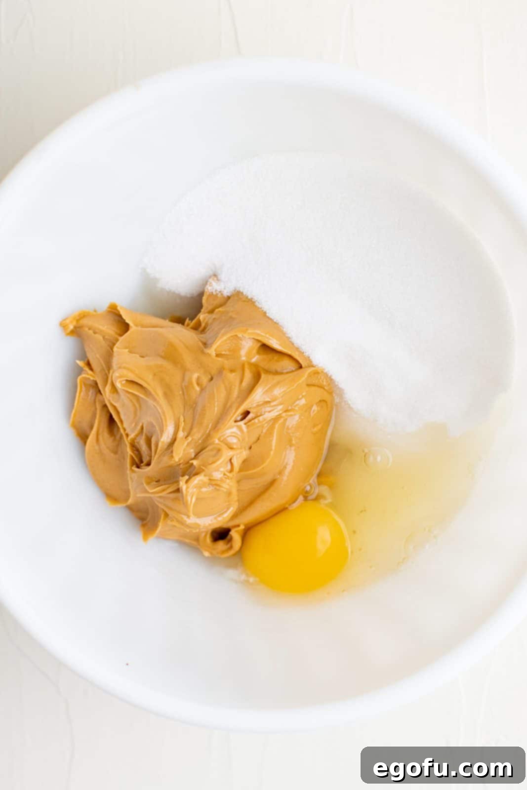A mixed bowl of peanut butter, sugar, and egg, showing the initial stage of cookie dough preparation.