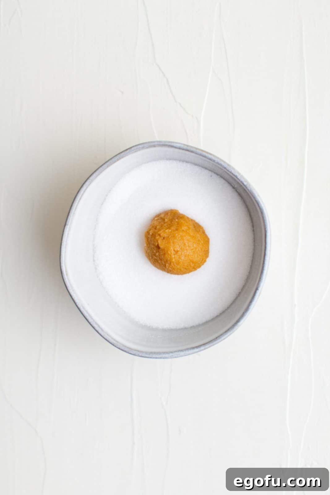 A single ball of 3-Ingredient Peanut Butter Cookie dough perfectly rolled in granulated sugar, ready for the baking sheet.