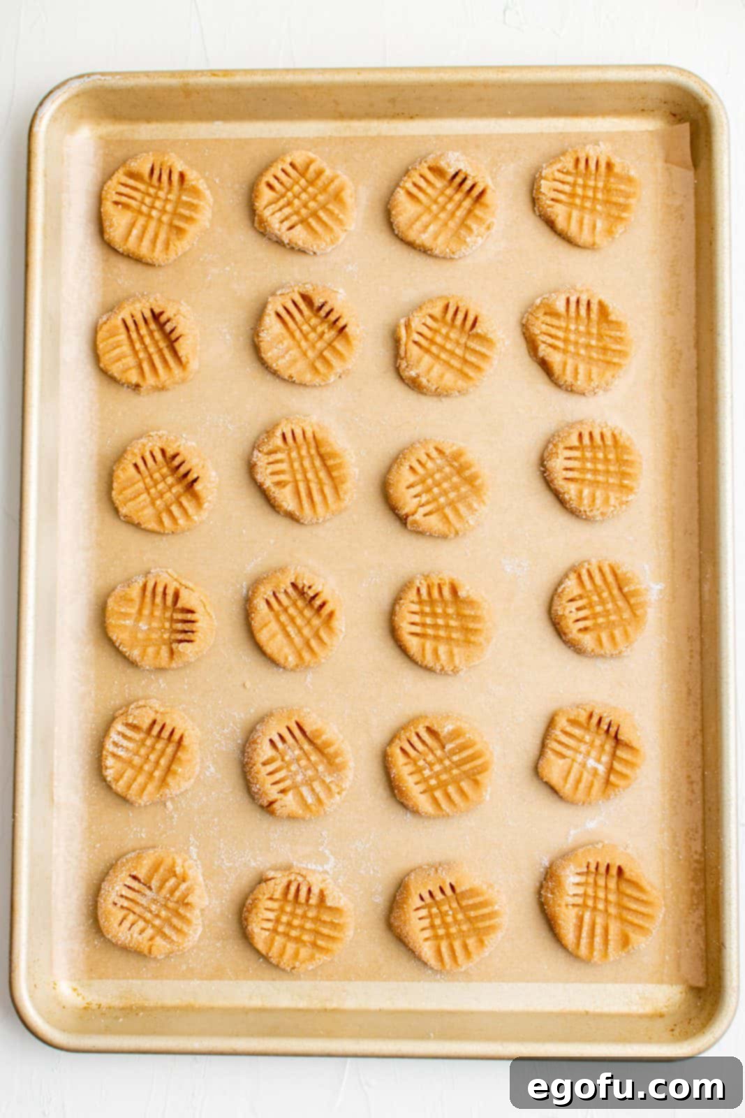 3-Ingredient Peanut Butter Cookies on a baking sheet, displaying the classic crosshatch pattern pressed with a fork before baking.