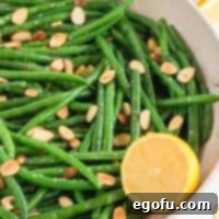 Square image of Almond Green Beans in bowl with half a lemon.