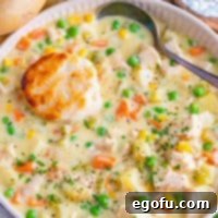Square close up overhead image of Chicken Pot Pie Soup in bowl with biscuit and spoon.