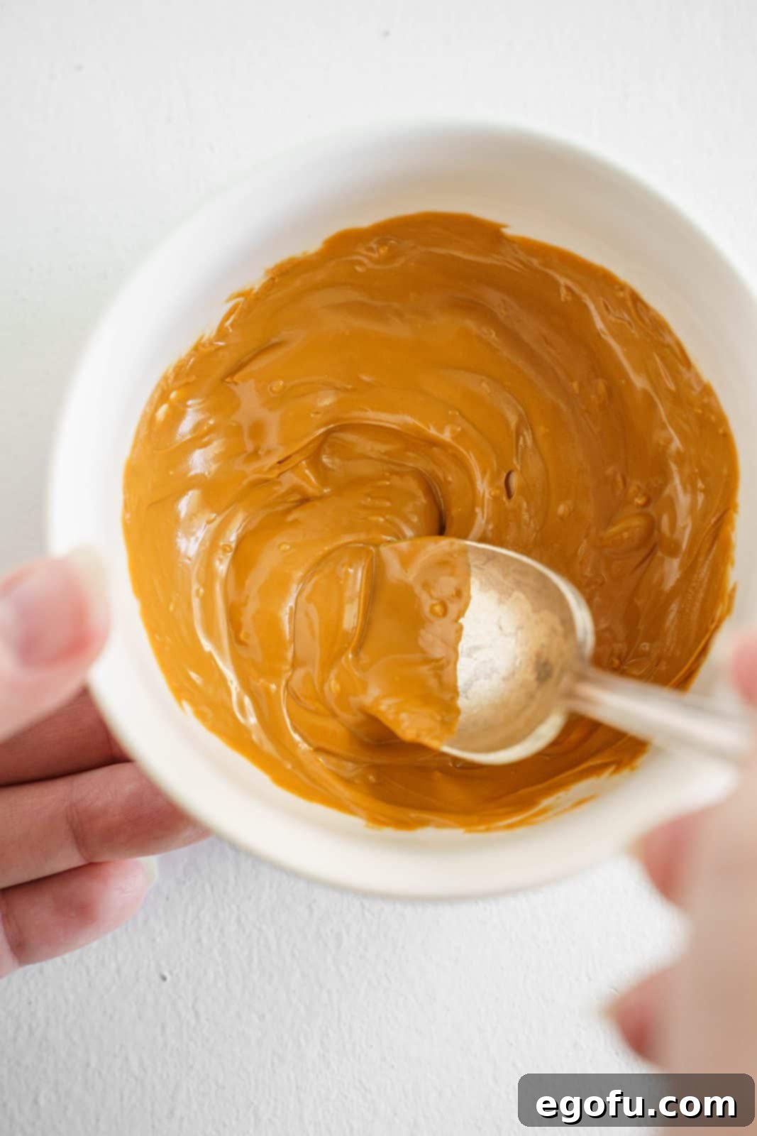 Spoon stirring melted peanut butter candy melts in white bowl.