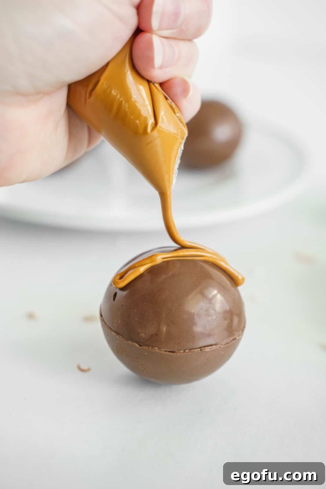 Peanut butter candy melts being piped over Hot Cocoa Bomb