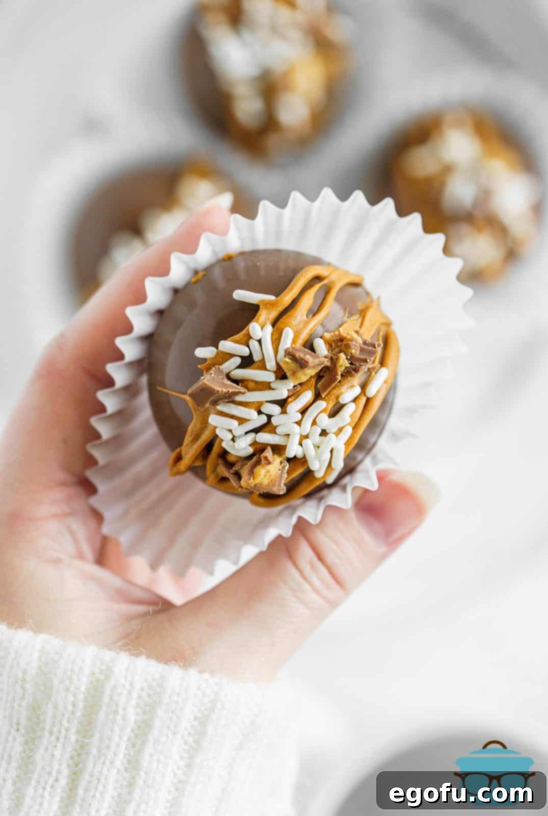 Hand holding one Chocolate Peanut Butter Hot Cocoa Bombs in paper liner.