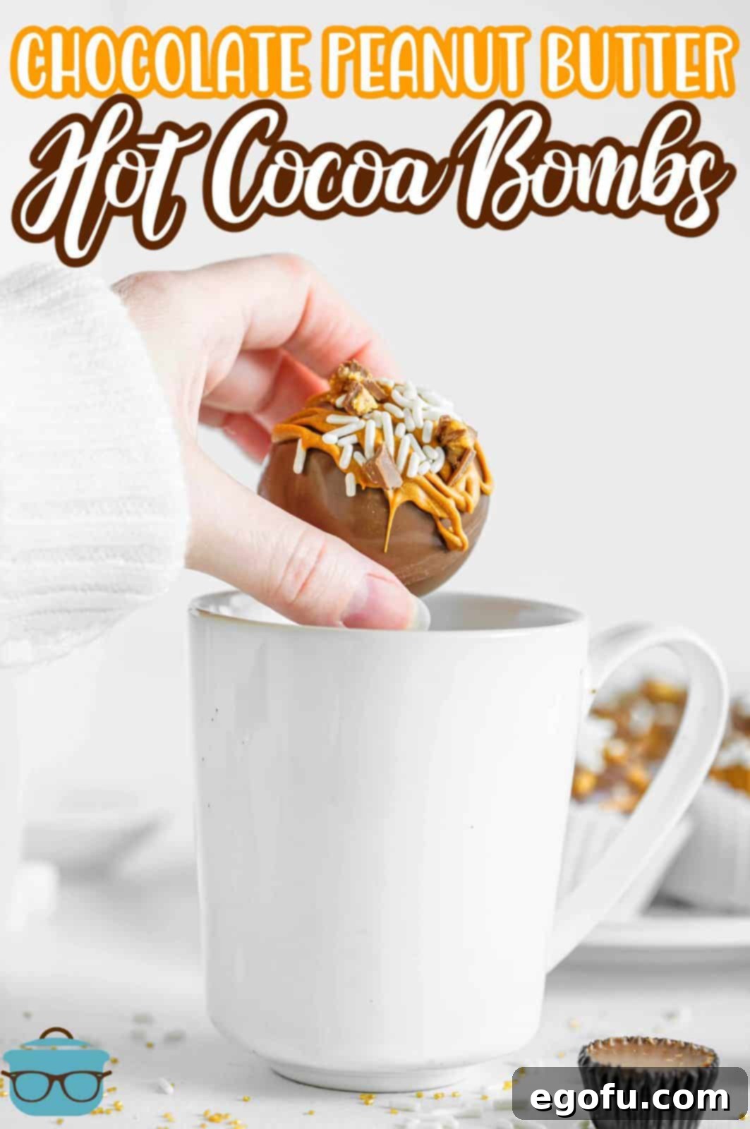 Pinterest image showing hand placing one Chocolate Peanut Butter Hot Cocoa Bombs into white mug.