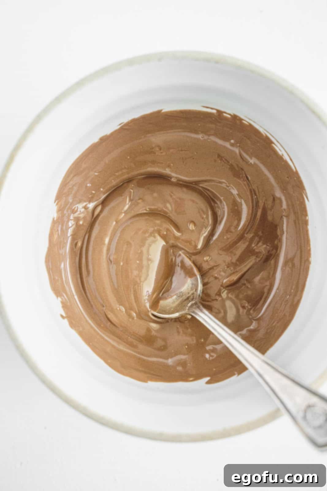 Chocolate candy melts being stirred melted in white bowl.