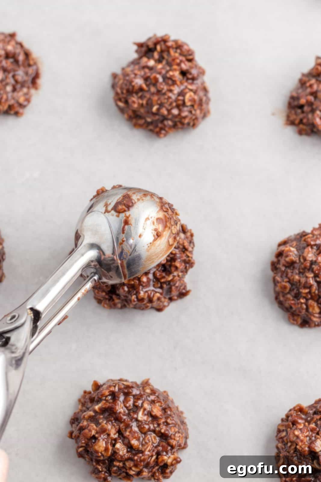 Cookie scoop dropping cookies onto parchment lined baking sheet to set up.