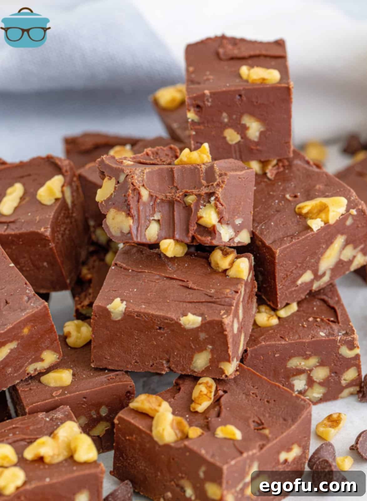 Stacked Chocolate Walnut Fudge on top of one another with a bite taken out of the top piece, showcasing its creamy texture and rich chocolate color.