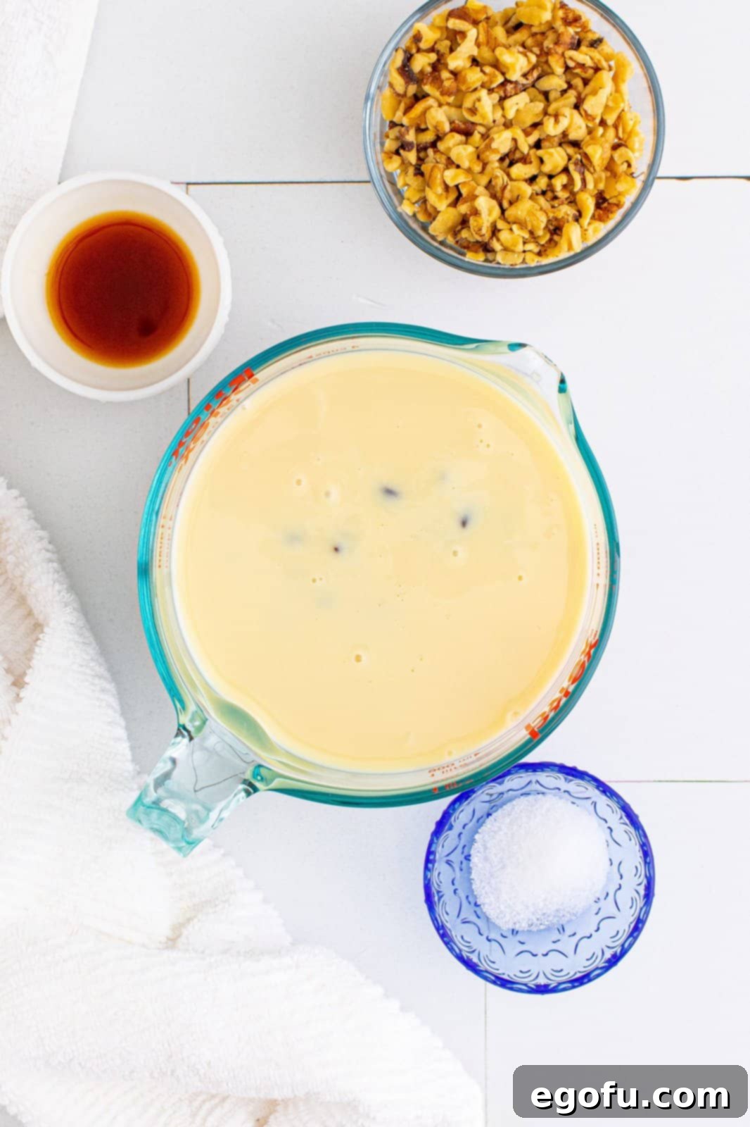 Semi-sweet chocolate chips in a large bowl with sweetened condensed milk being poured over them from a measuring cup.