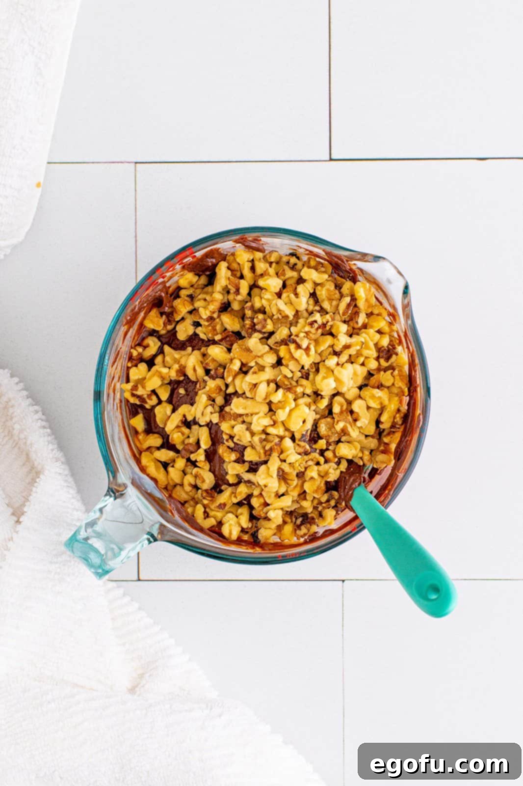 Vanilla extract, salt, and three-quarters of the chopped walnuts being added to the melted fudge mixture and stirred in.