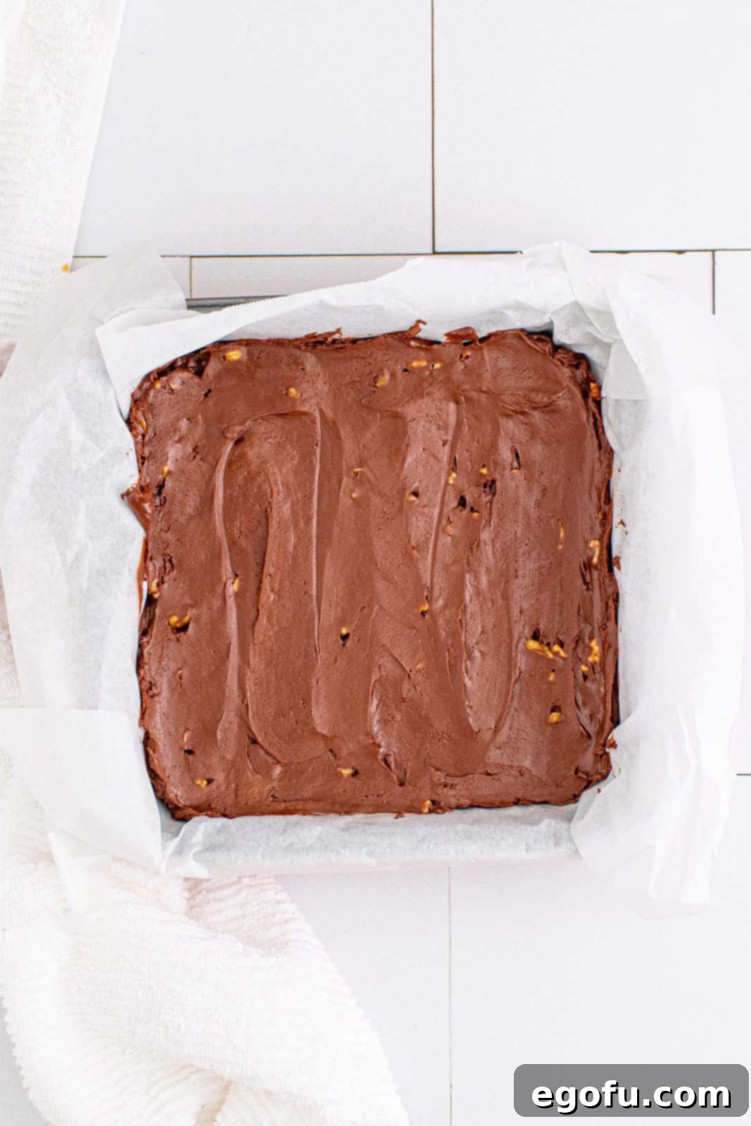 The warm fudge mixture spread evenly into a parchment-lined baking pan, ready for the final touches.