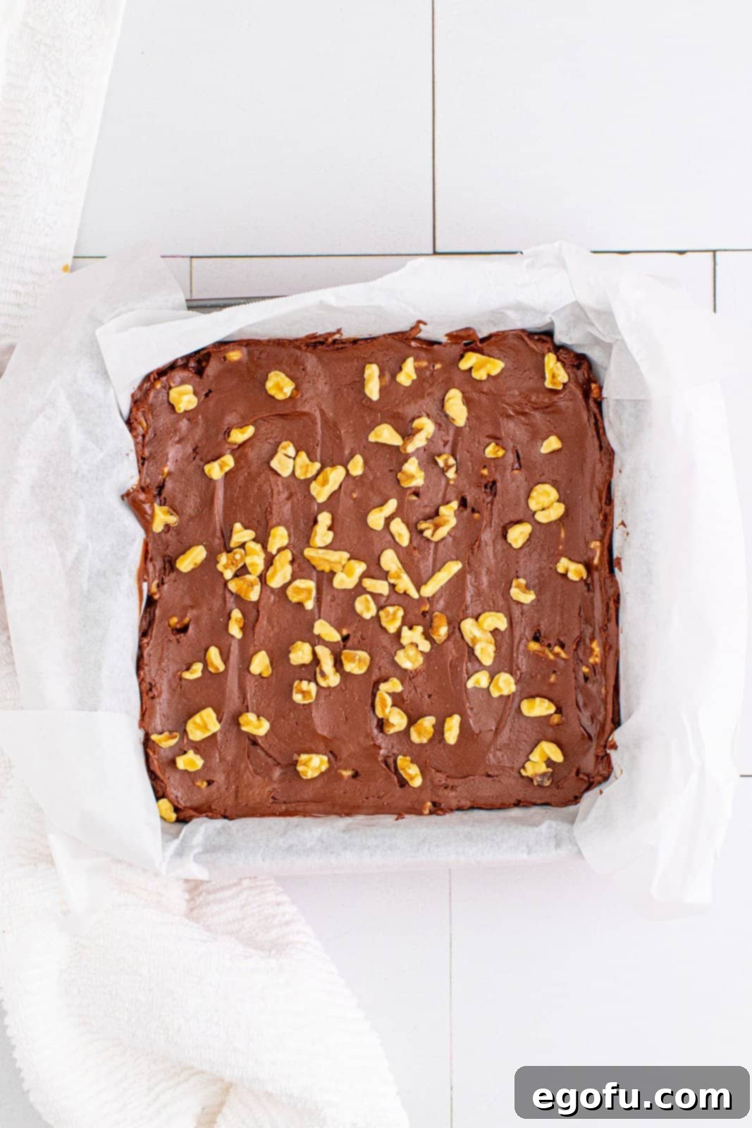 Remaining chopped walnuts scattered and gently pressed onto the top of the smooth fudge mixture in the pan.