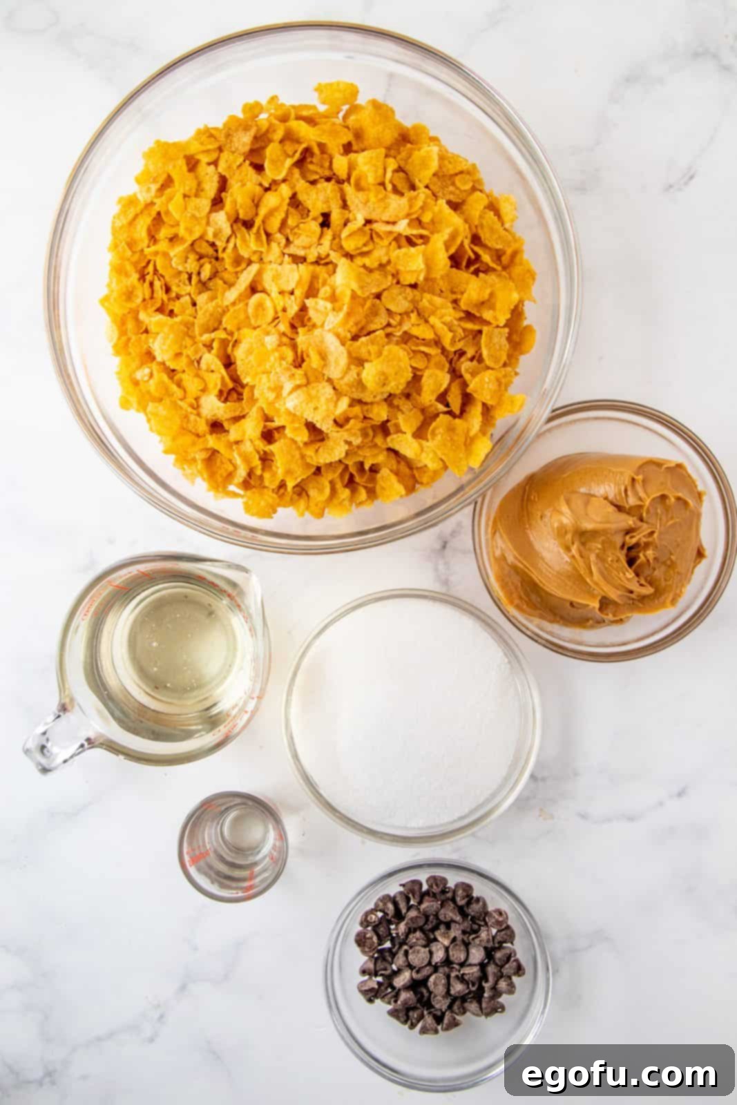 Grandmas Effortless No Bake Cornflake Delights 4 All the necessary ingredients laid out for making cornflake cookies: cornflakes, light corn syrup, sugar, creamy peanut butter, vanilla extract, chocolate chips, and oil.