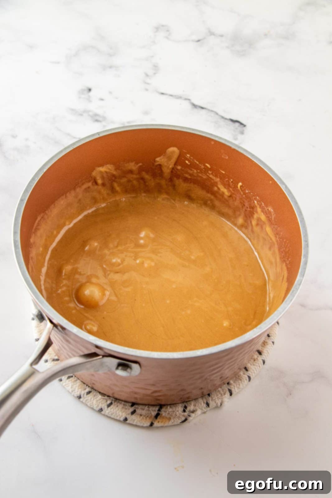 Grandmas Effortless No Bake Cornflake Delights 7 Creamy peanut butter and vanilla extract being stirred into the warm corn syrup and sugar mixture until smooth and well combined.