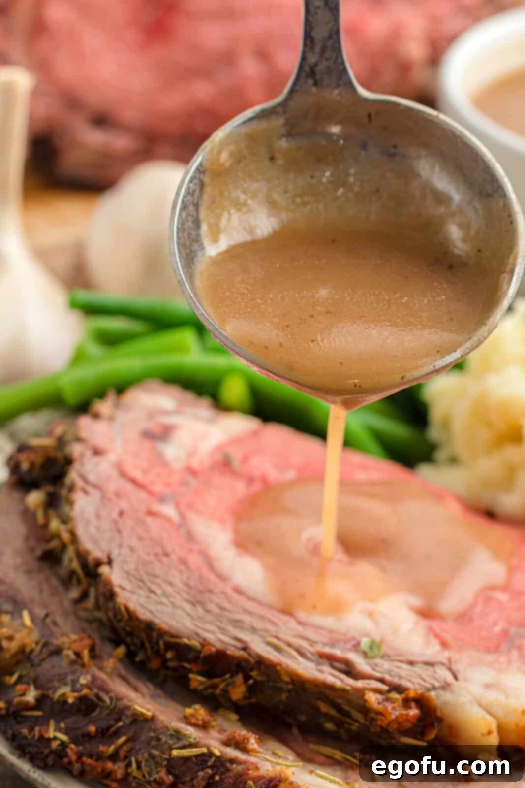 A ladle gracefully spooning rich au jus over a delectable slice of Garlic Butter Prime Rib, highlighting its juiciness.