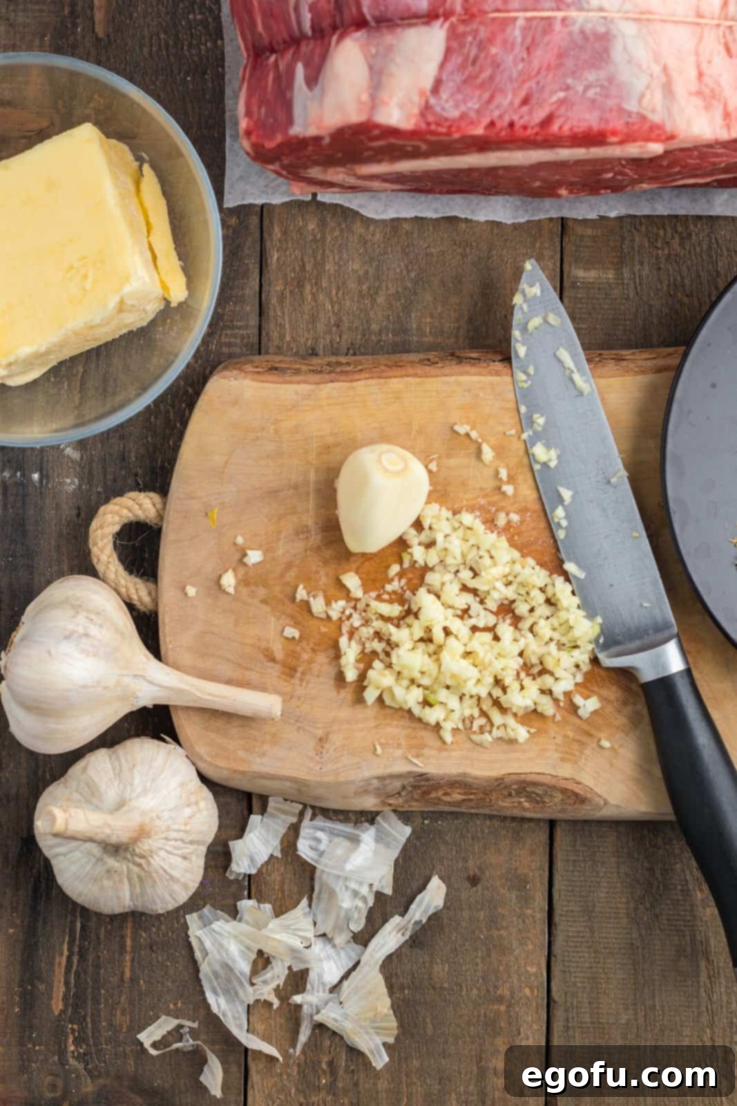 Fresh garlic cloves being finely chopped on a wooden cutting board, ready for the herb butter mixture.