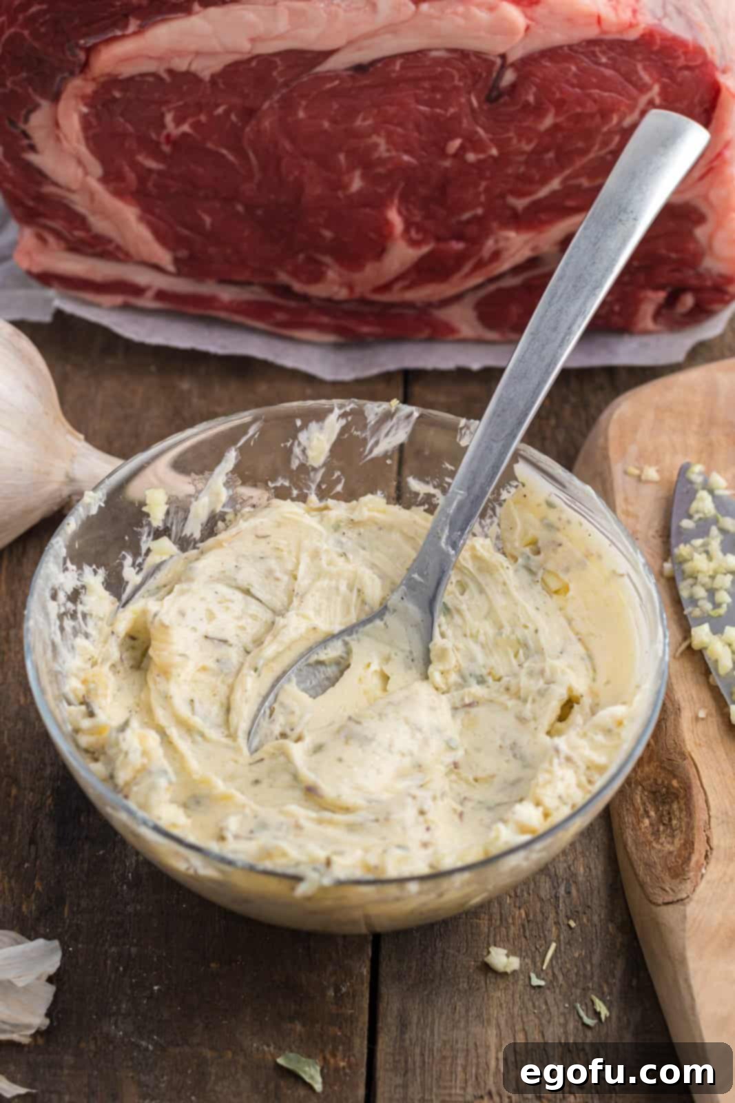 A close-up of butter, minced garlic, and various dried herbs beautifully combined in a small bowl.
