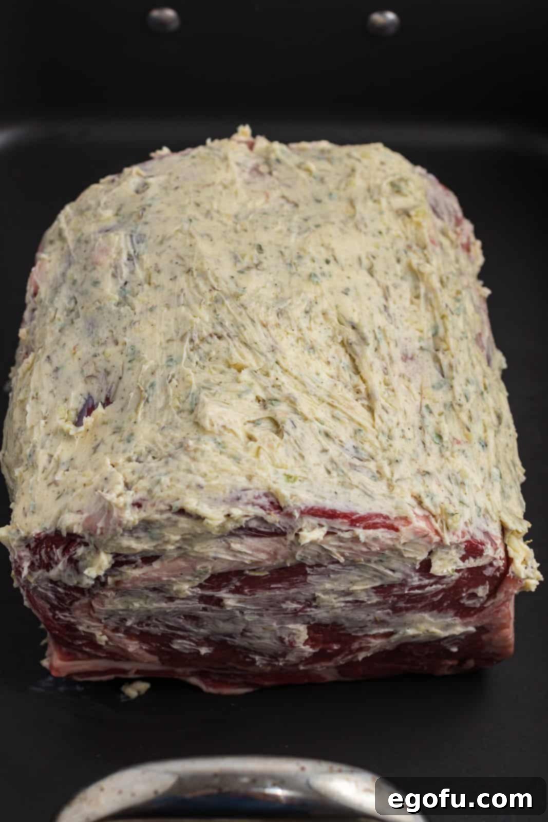 A prime rib roast generously coated with the fragrant garlic herb butter mixture, ready for the oven.