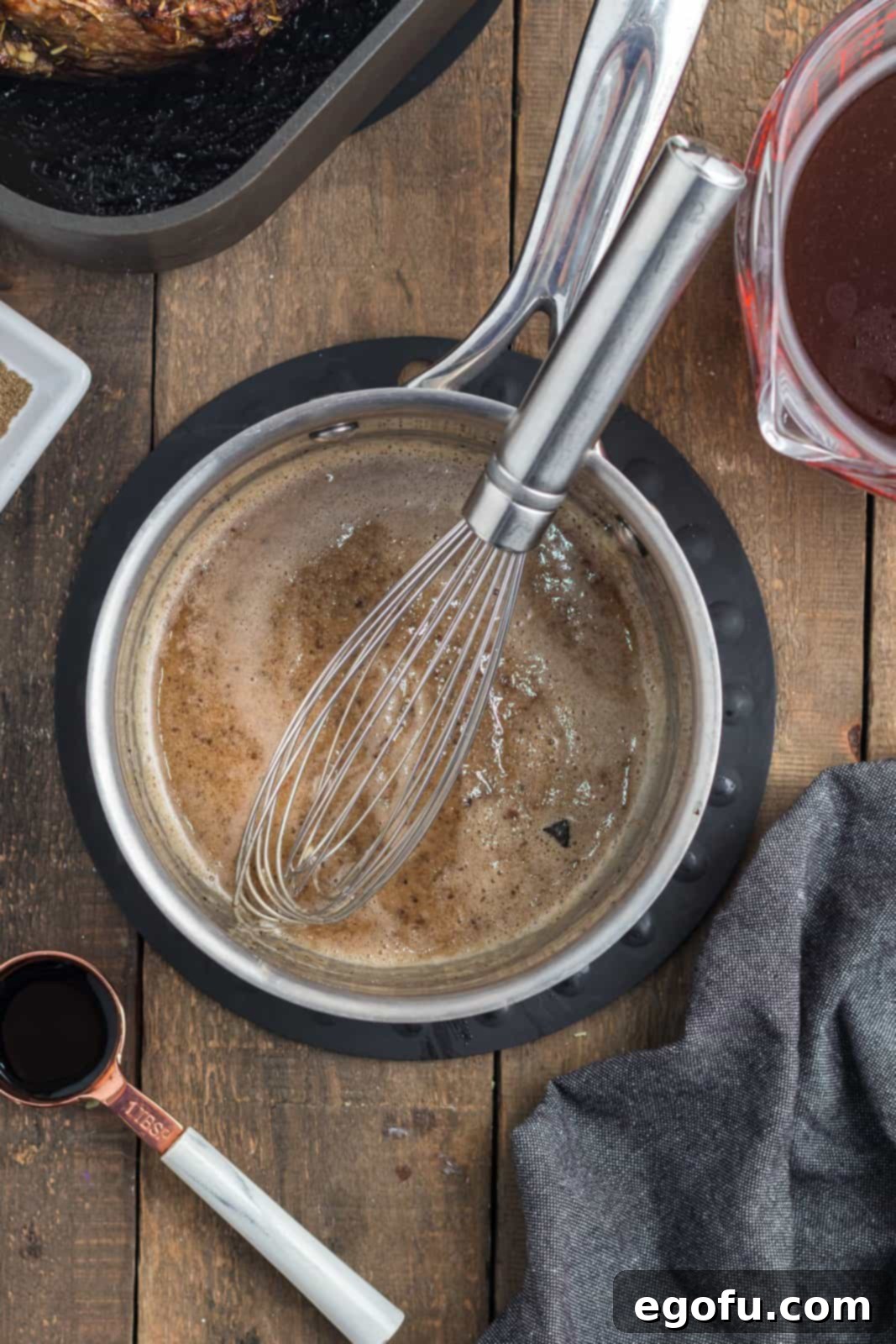 Beef drippings being whisked vigorously with all-purpose flour in a saucepan to create a flavorful roux for the au jus.