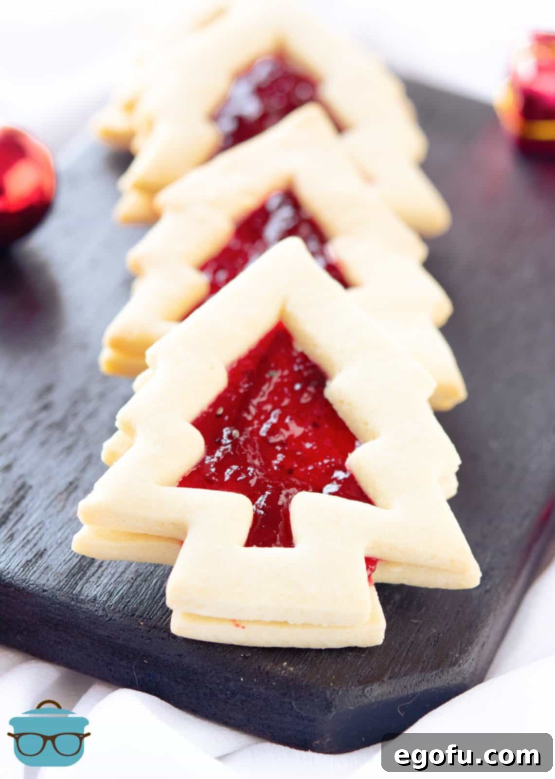 Christmas Tree Linzer Cookies layered on top of one another on black platterr.