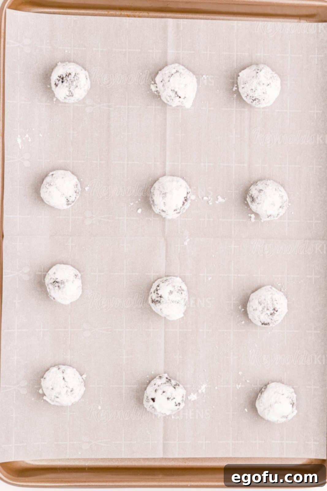 Cookie dough rolled in powdered sugar on parchment lined sheet pan.