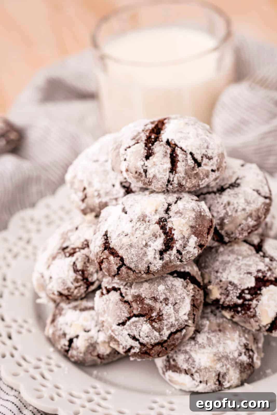 Stacked Chocolate Crinkle Cookies on white plate with milk in background.