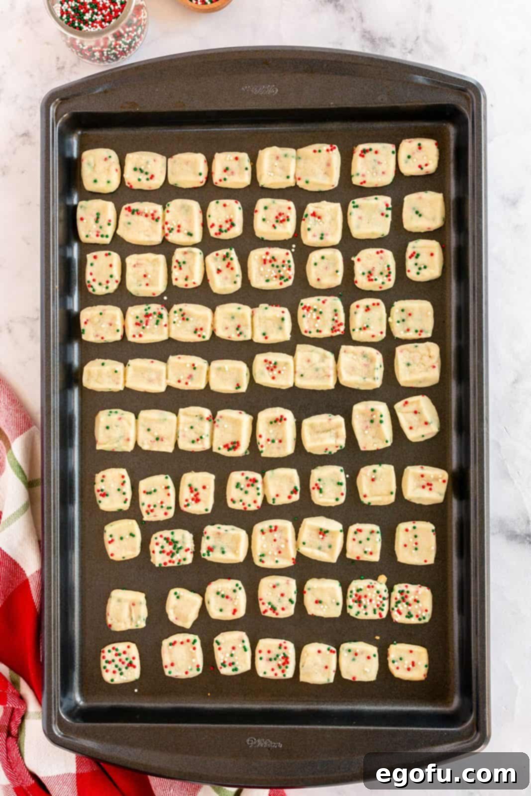 Freshly baked Mini Christmas Shortbread Cookies cooling on a baking sheet, with their vibrant sprinkles intact.