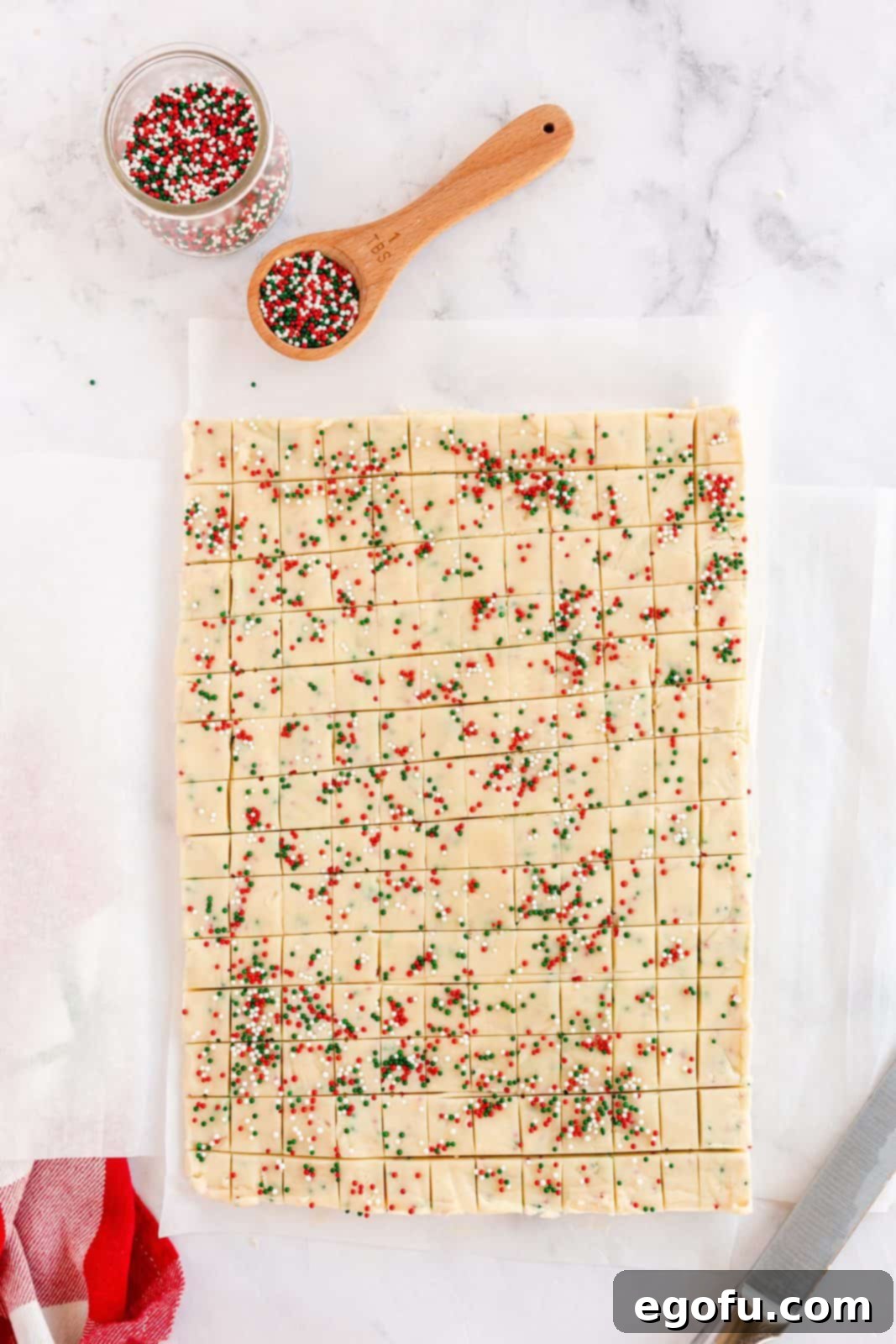 Chilled shortbread dough expertly cut into small, uniform squares on parchment paper.