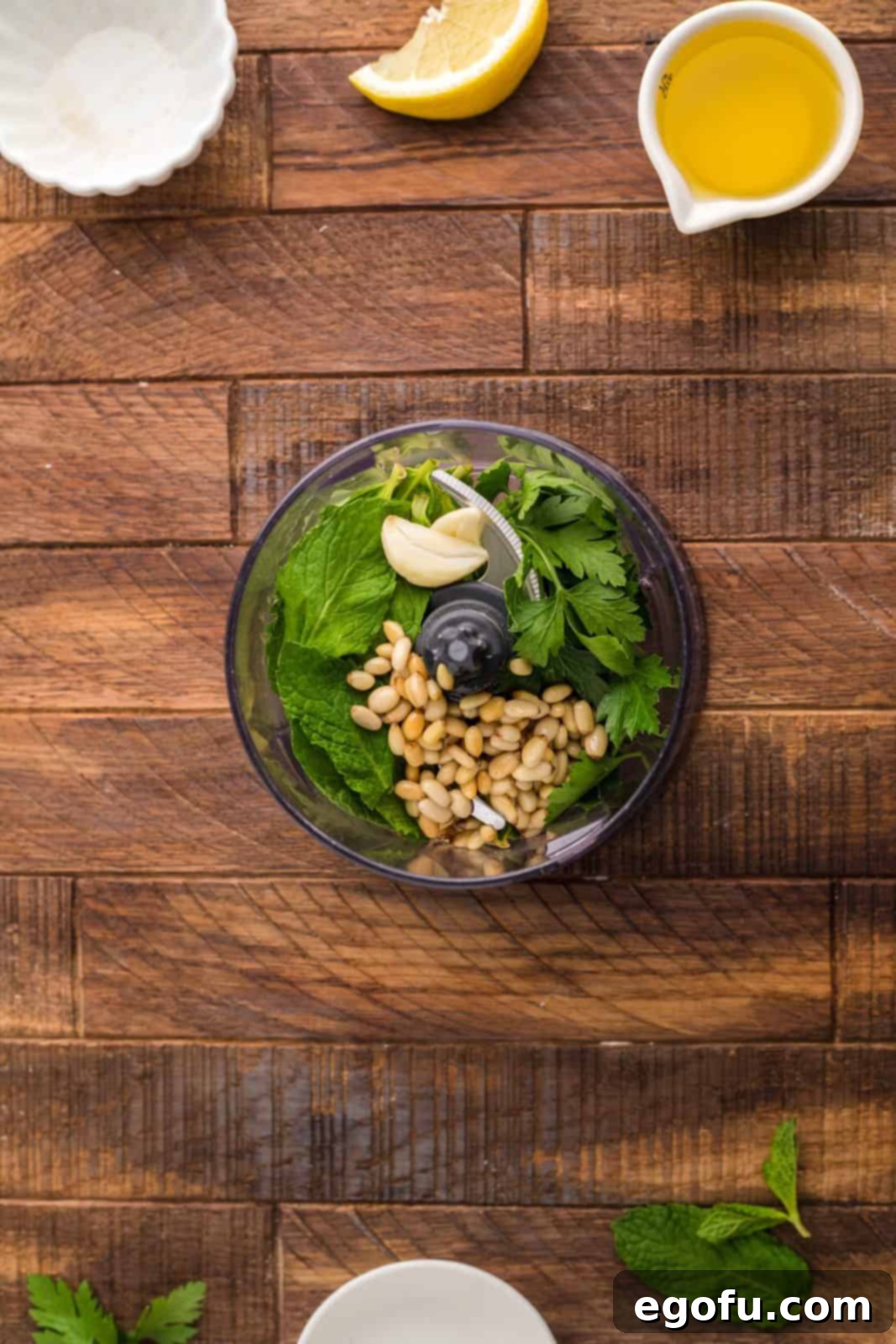 Succulent Lamb Chops 11 All mint pesto ingredients – toasted pine nuts, fresh mint and parsley, minced garlic, lemon juice, and olive oil – gathered in a food processor bowl, ready for blending.