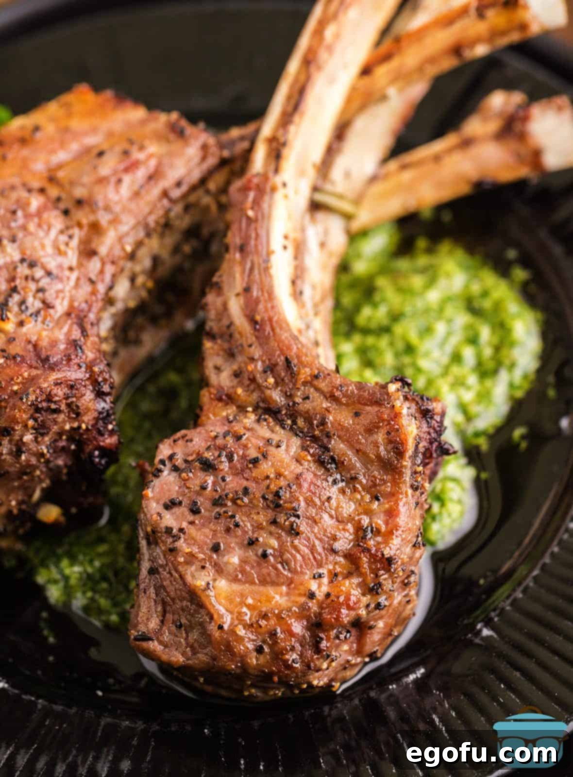 Succulent Lamb Chops 14 A perfectly plated Lamb Chop resting atop a vibrant dollop of Mint Pesto on a sleek black plate, ready to be enjoyed.