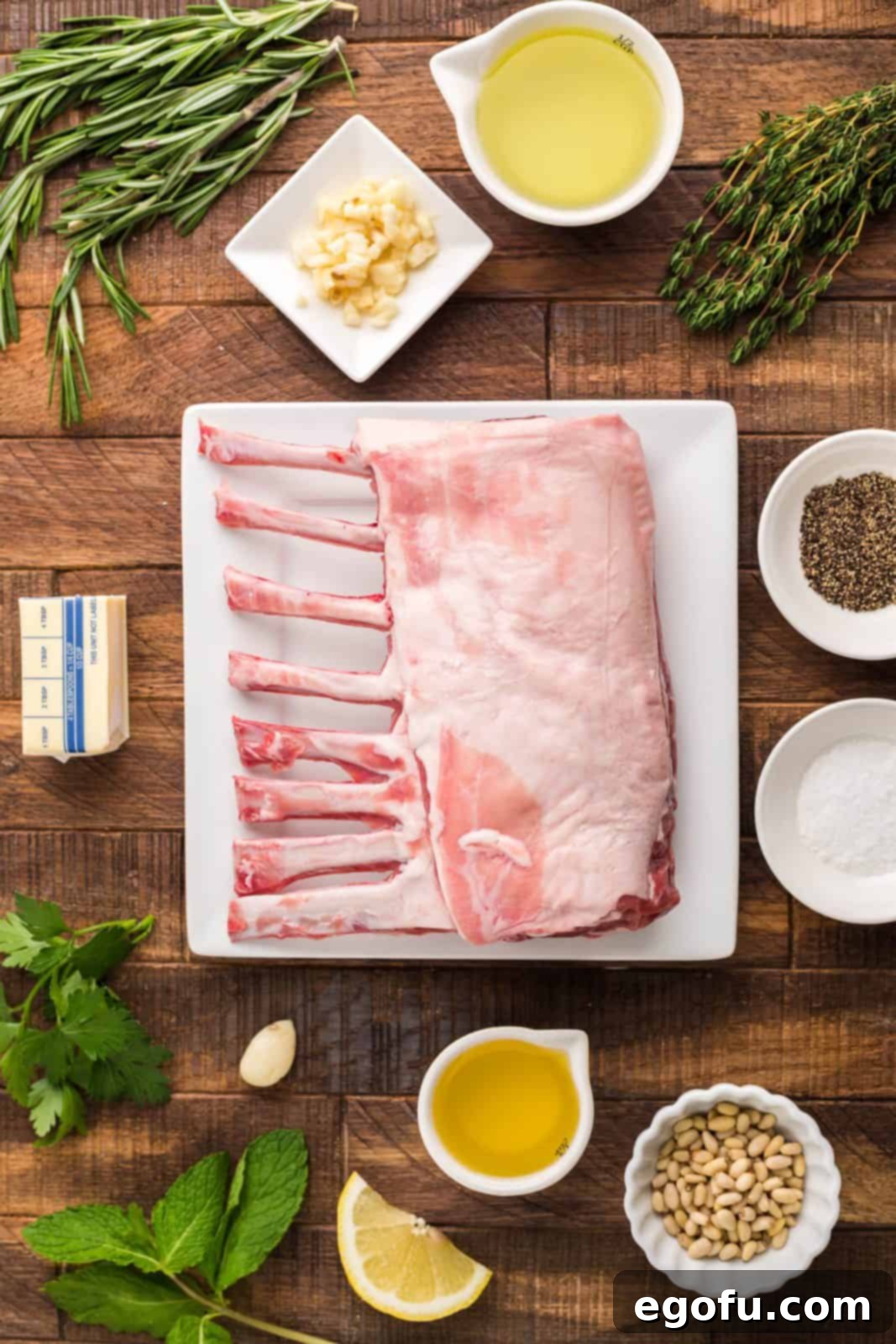 Succulent Lamb Chops 4 A curated display of all essential ingredients: a beautiful rack of lamb, bottles of grapeseed and olive oil, fresh sprigs of rosemary and thyme, plump garlic cloves, pine nuts, vibrant mint and parsley leaves, a lemon, and a block of salted butter.