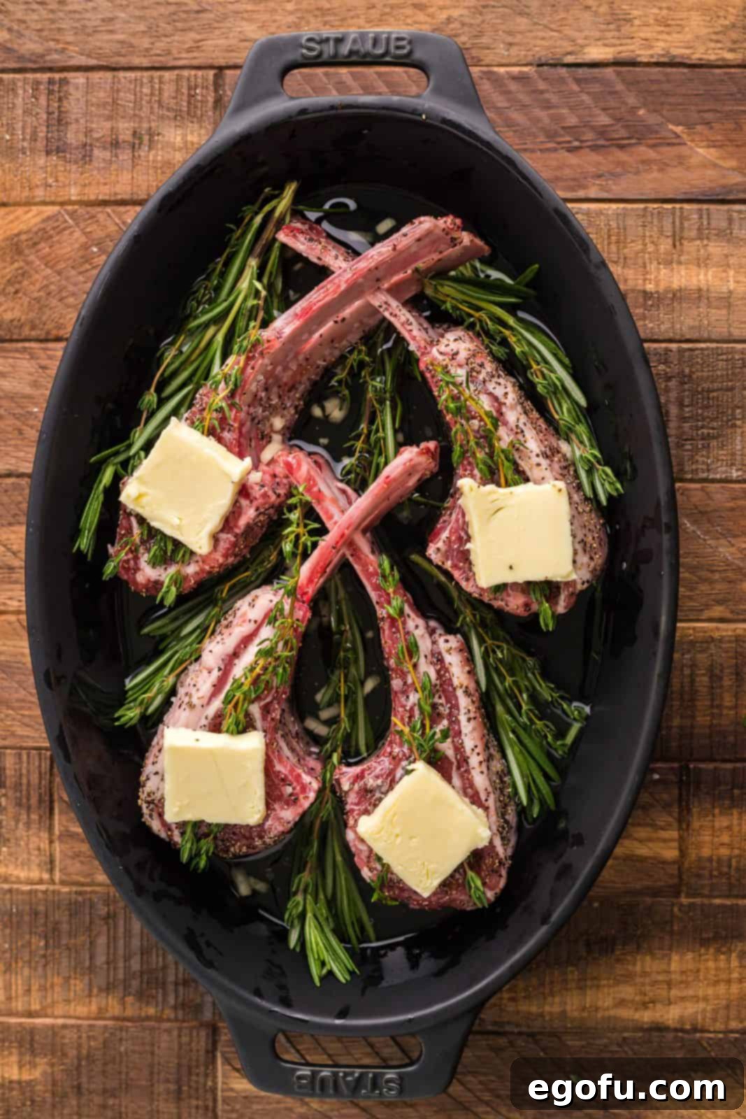 Succulent Lamb Chops 8 Marinated lamb chops arranged aesthetically in an oven-safe pan, topped with fresh thyme sprigs and slices of salted butter, ready for broiling.