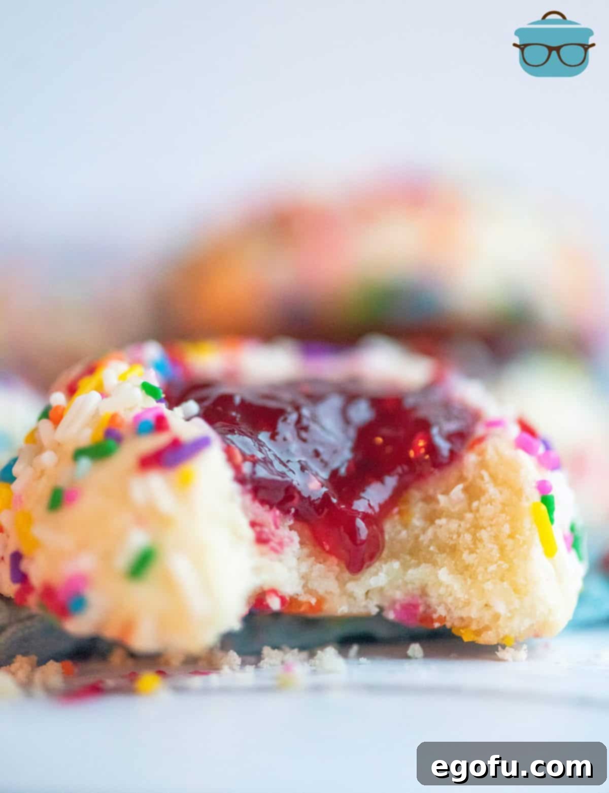 A beautifully baked Raspberry Thumbprint Cookie with a bite taken out, revealing the soft interior and luscious raspberry jam.