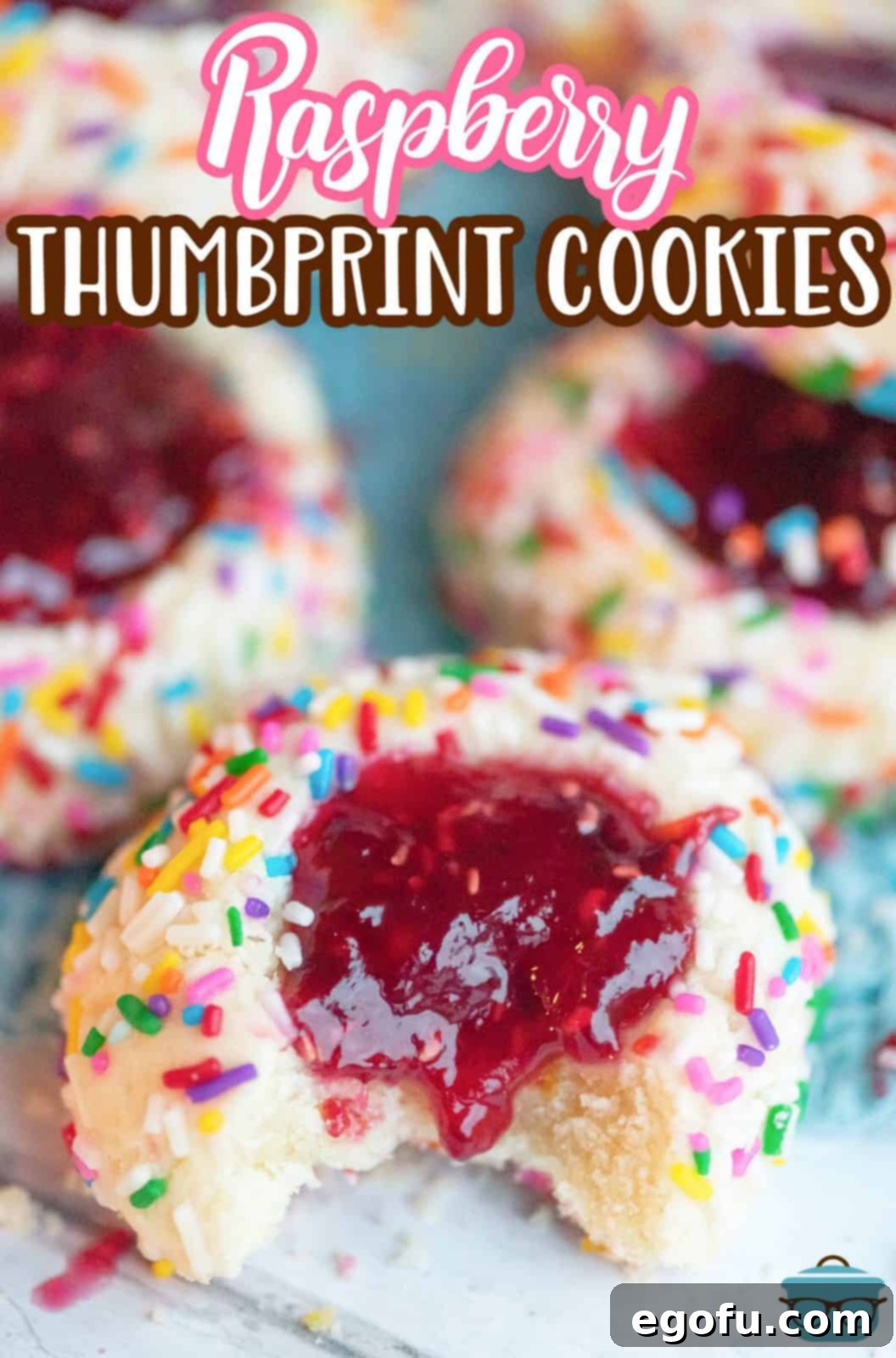 A beautiful overhead shot of Raspberry Thumbprint Cookies, one with a bite taken out, showcasing the rich jam filling.