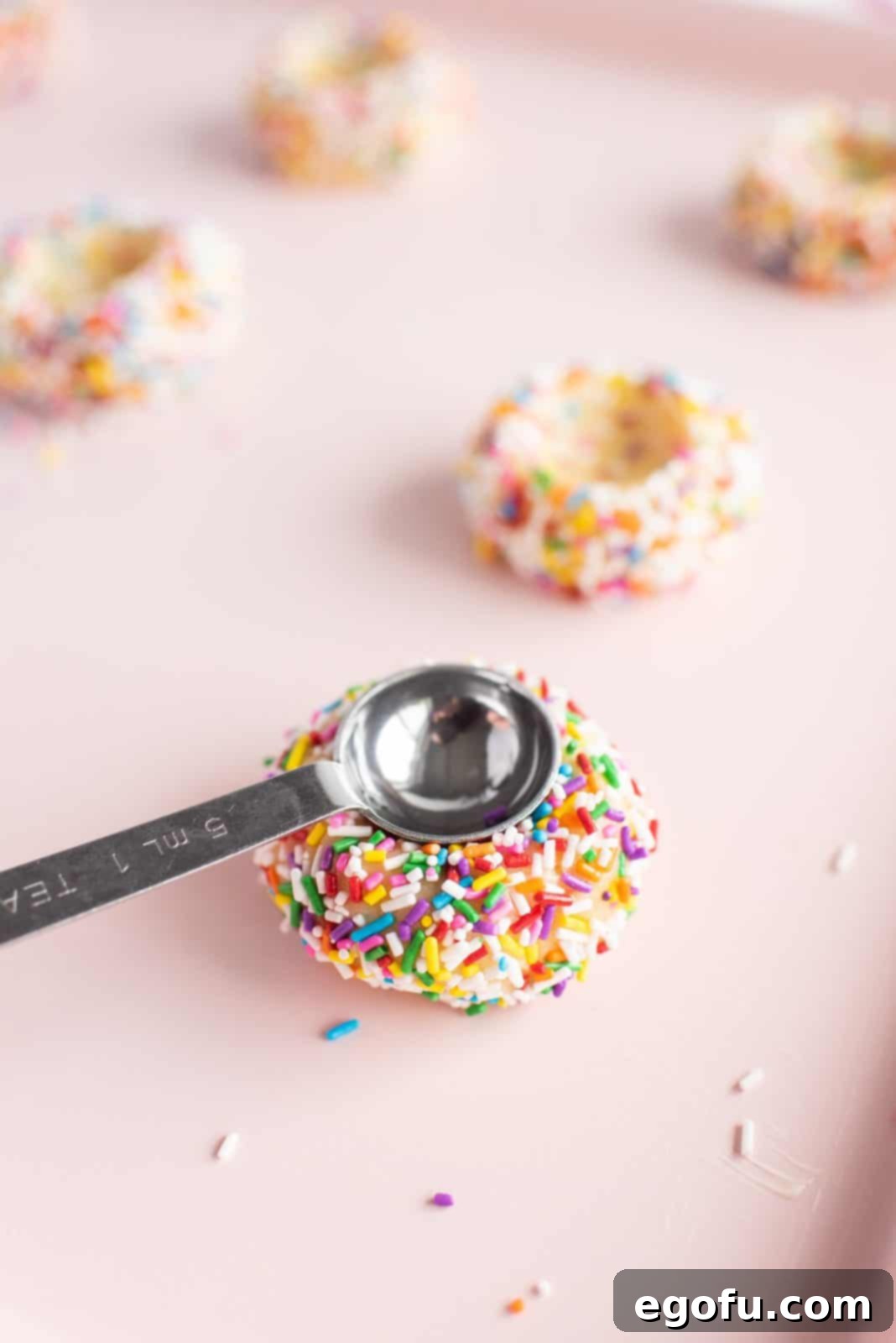 Indents being pressed into the center of unbaked cookie dough balls on a baking sheet, ready for filling.