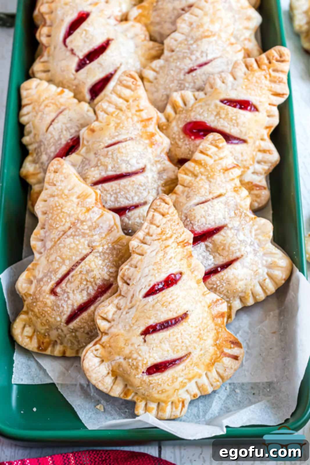 Overhead photo of Christmas Tree Hand Pies on platter layered on top of one another. Golden-brown crusts with visible cherry filling hints, topped with sanding sugar.