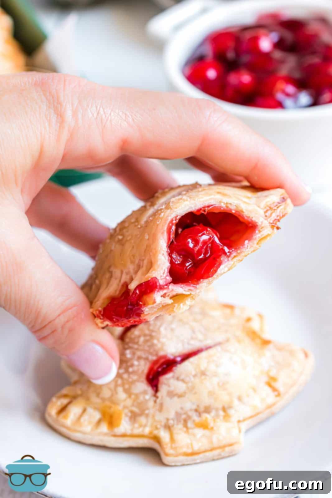 Hand holding up one Christmas Tree Hand Pie with bite taken out showing the red cherry filling in center.