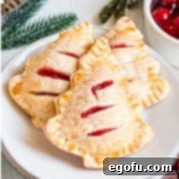 Square image of three Christmas Tree Hand pie on white plate. Golden crusts, visible cherry filling, and white sanding sugar. Ready to serve.