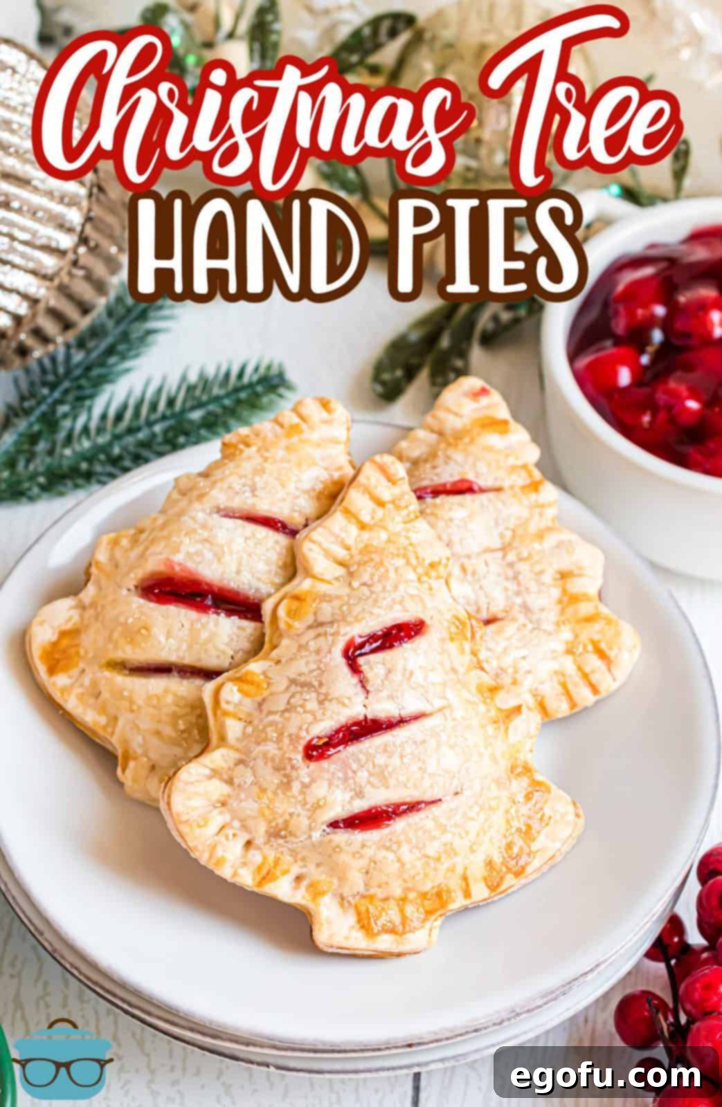 Pinterest image of three Christmas Tree Hand Pies on white plate. Golden crusts, visible cherry filling, and white sanding sugar. Ready to serve.