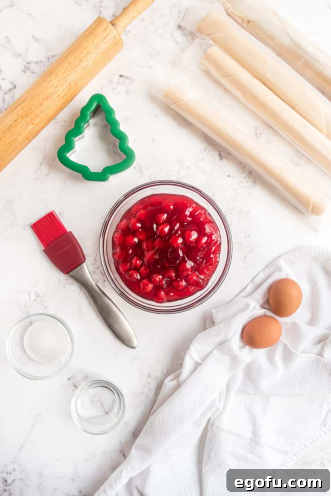 Ingredients needed: refrigerated pie crust, cherry pie filling, eggs, water and coarse sanding sugar displayed on a kitchen counter.