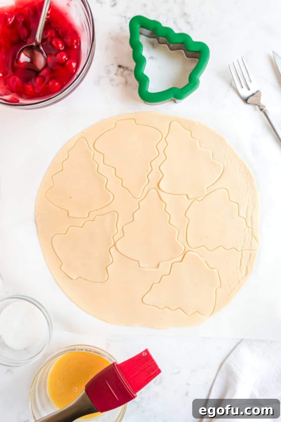 Christmas trees being cut out of pie crust using a festive cookie cutter.