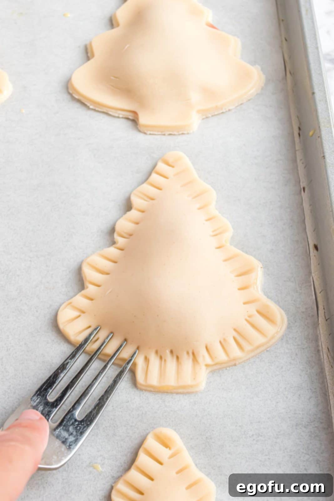 Fork sealing edges of top and bottom pie crust together, creating a crimped border on a Christmas tree hand pie.