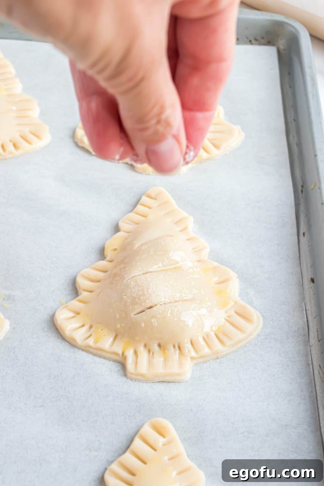 Sanding sugar being sprinkled on top of hand pies before baking, adding a festive sparkle.