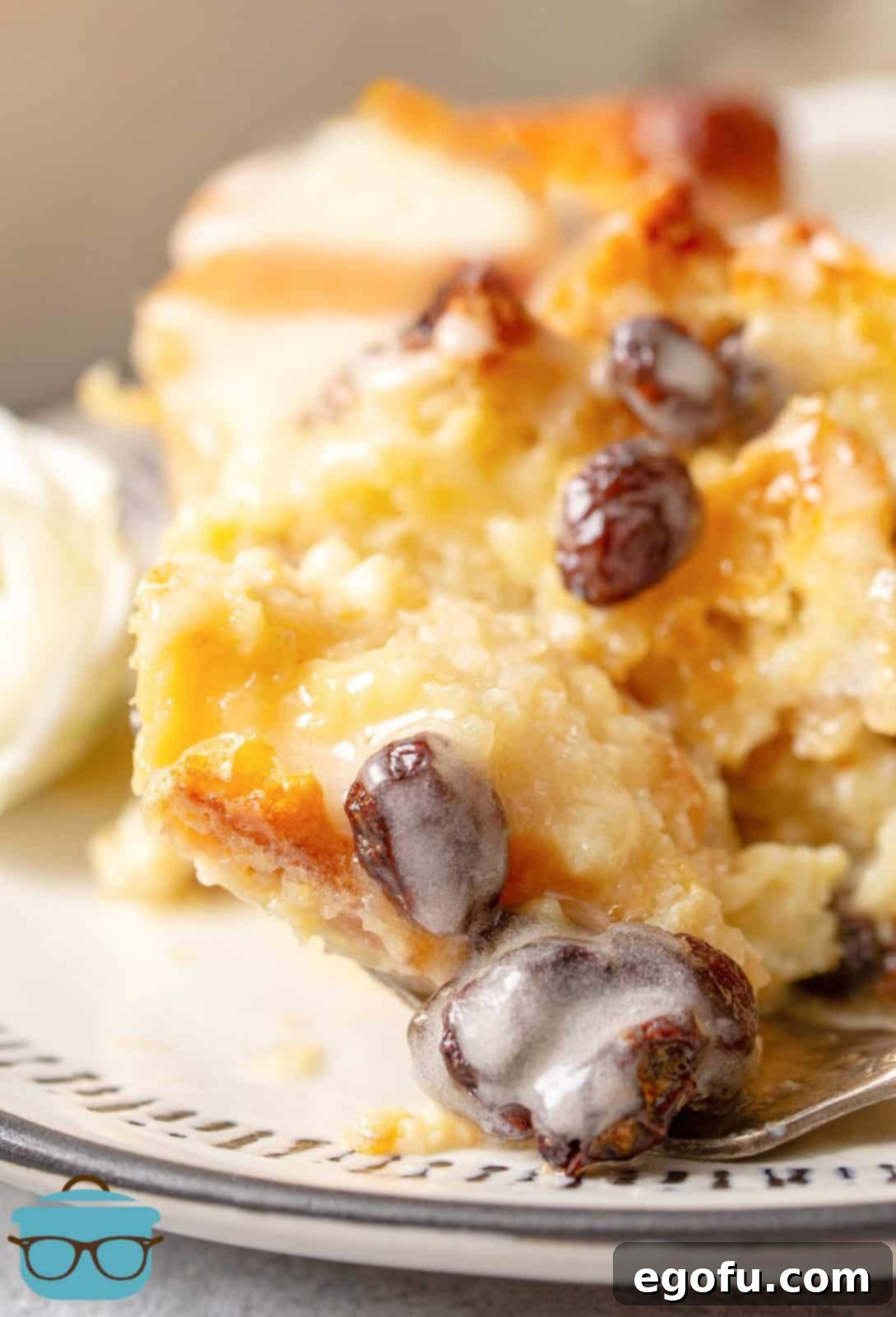 Close up of a slice of classic bread pudding, rich with custard and plump raisins, generously coated in a sweet, golden sauce.