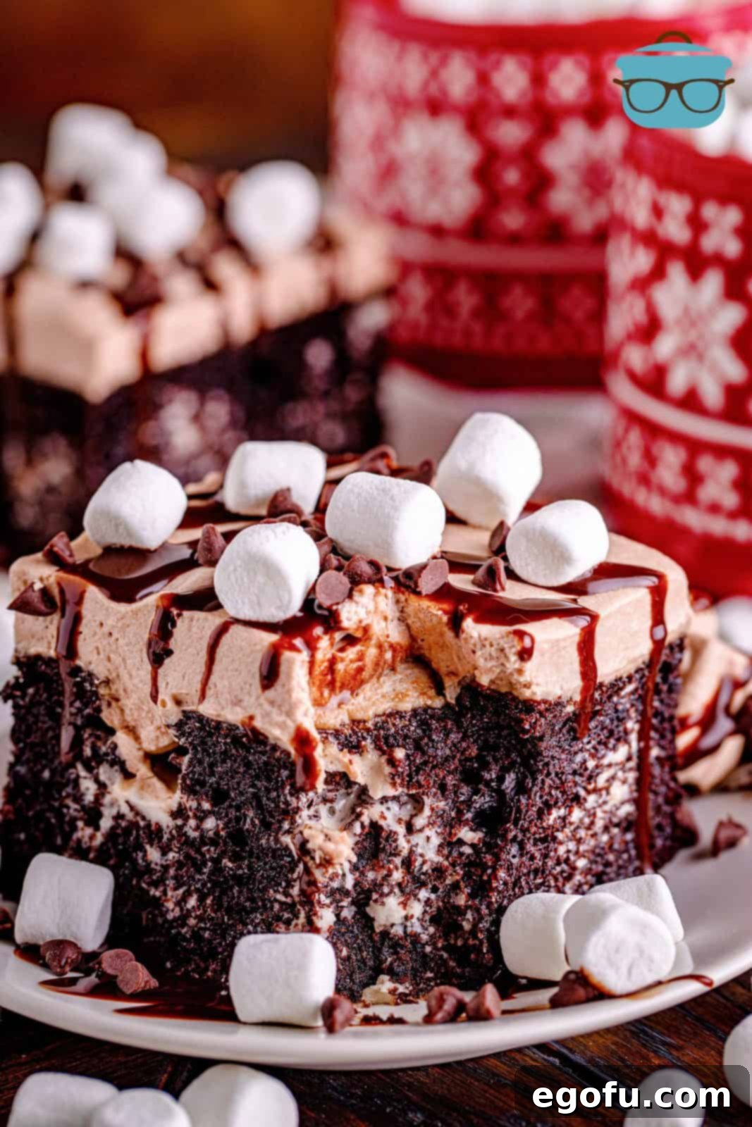 slice of hot chocolate poke cake on a white plate with two red mugs in the background.