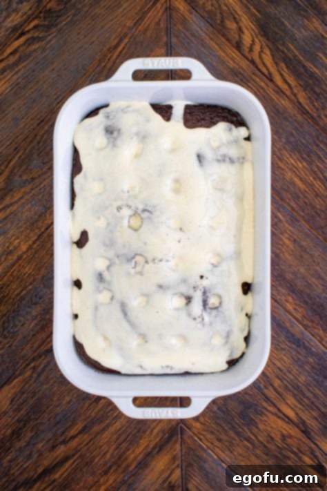 melted marshmallow mixture shown spread on top of cake that has holes poked in it.